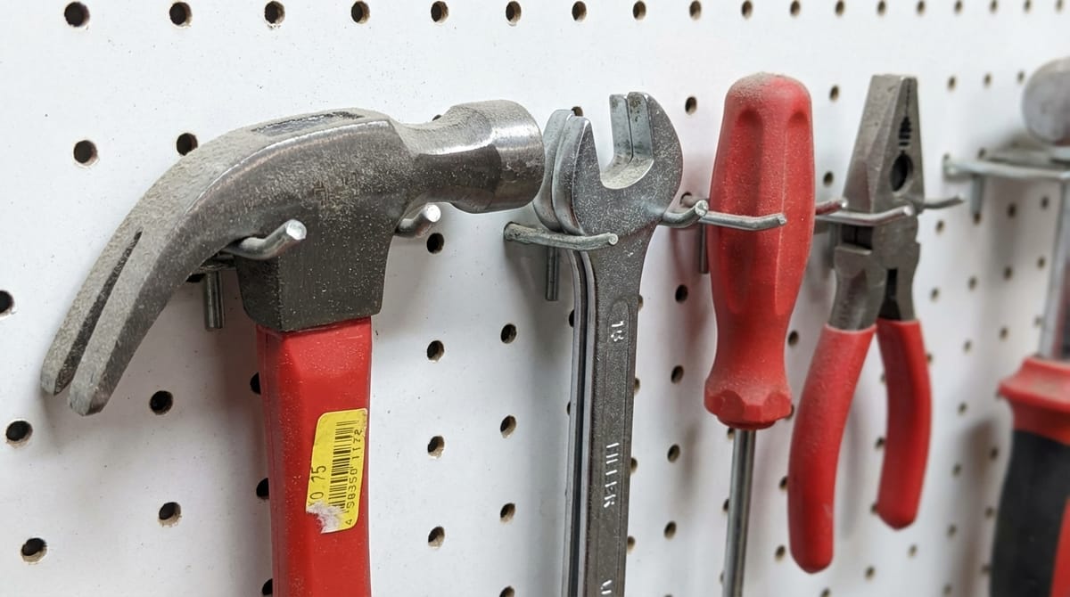 Tools hanging on a pegboard — a claw hammer, adjustable wrench, screwdriver, and pliers — organized and available but untouched.